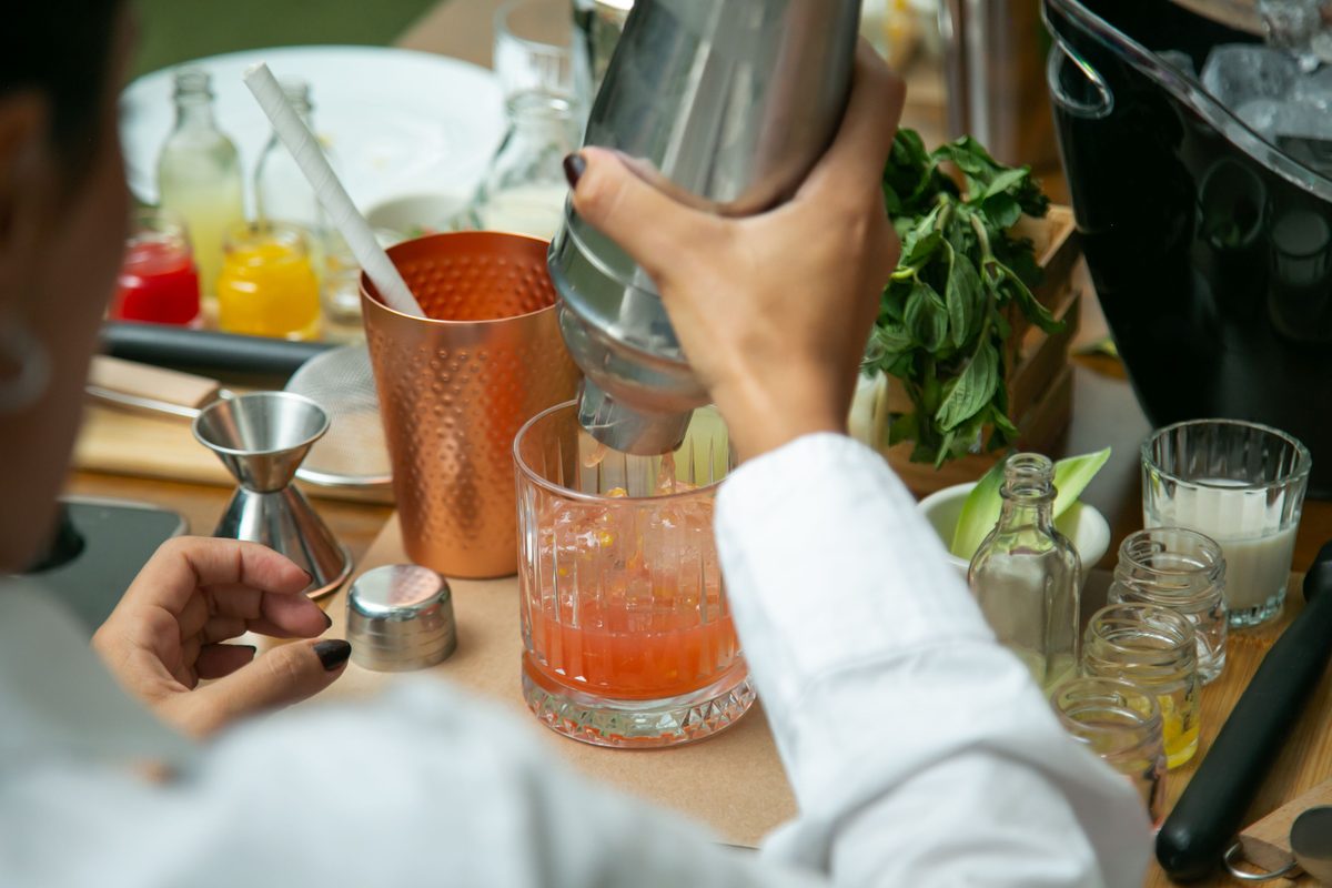 A bartender shaking a cocktail beside a copper cup and fresh herbs