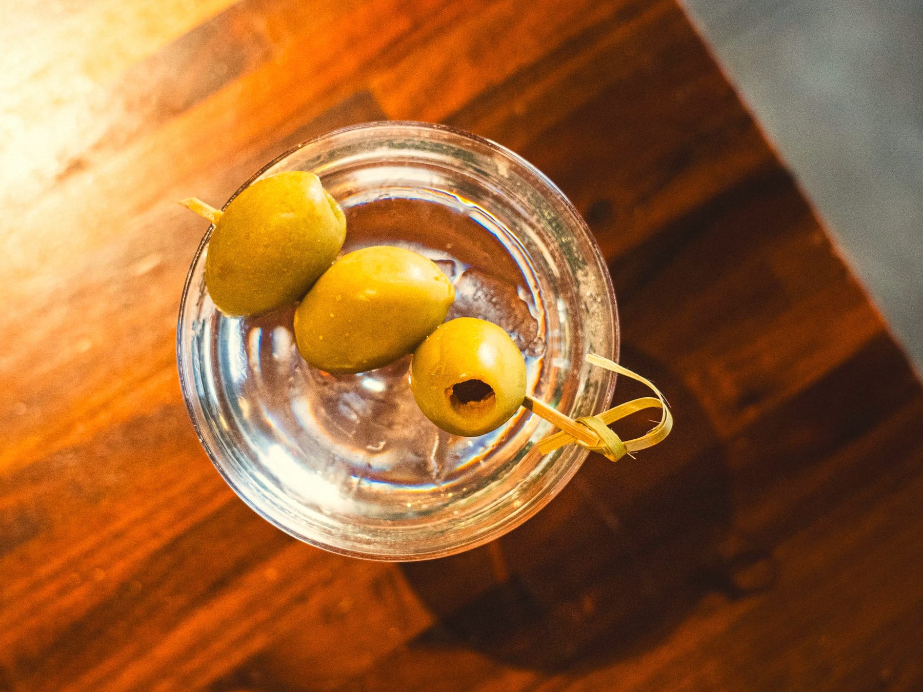 Overhead view of a clear martini with three green olives on a cocktail pick