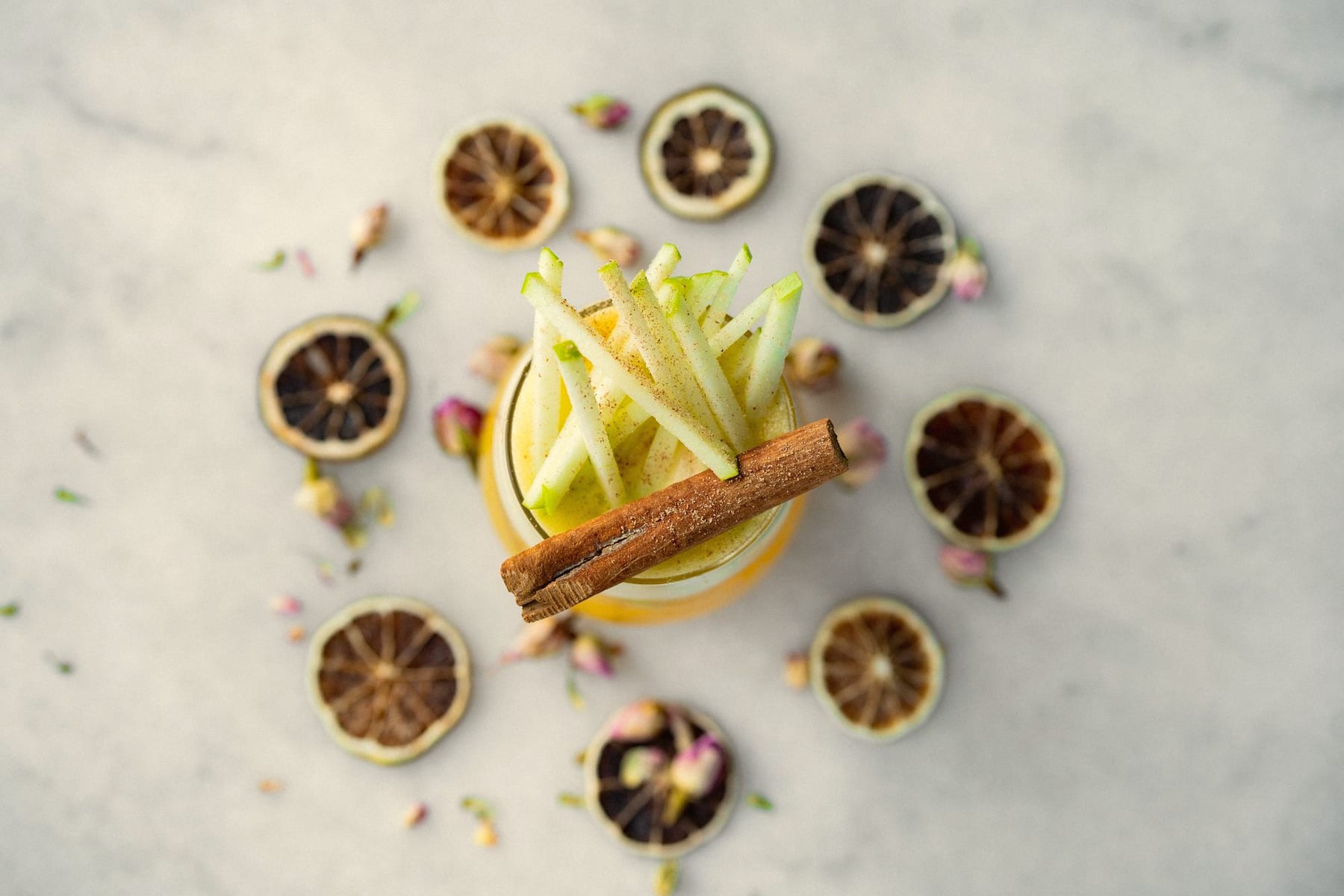 Overhead view of a cocktail topped with apple matchsticks and cinnamon, ringed by dried lime slices
