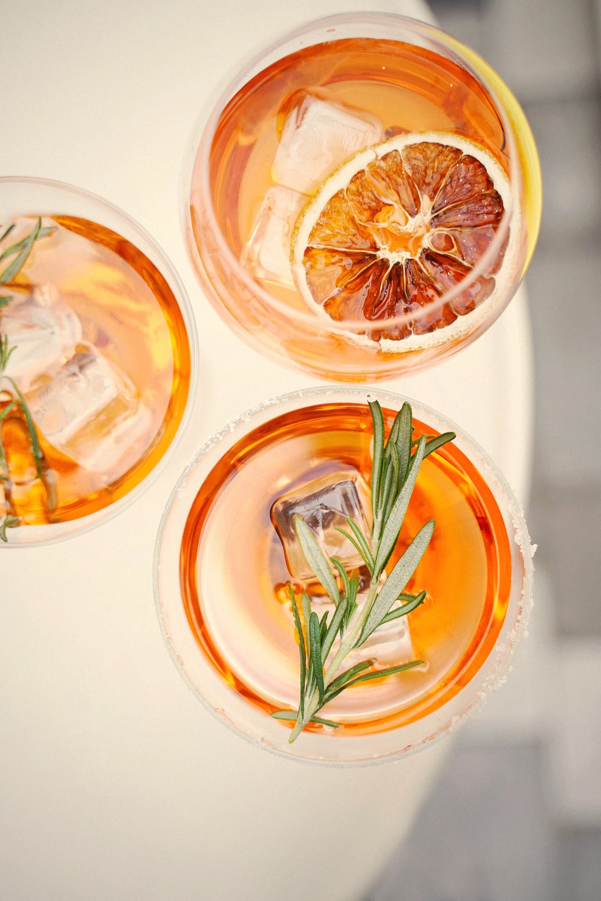 Overhead view of three orange cocktails with ice, rosemary sprigs and a dried orange slice