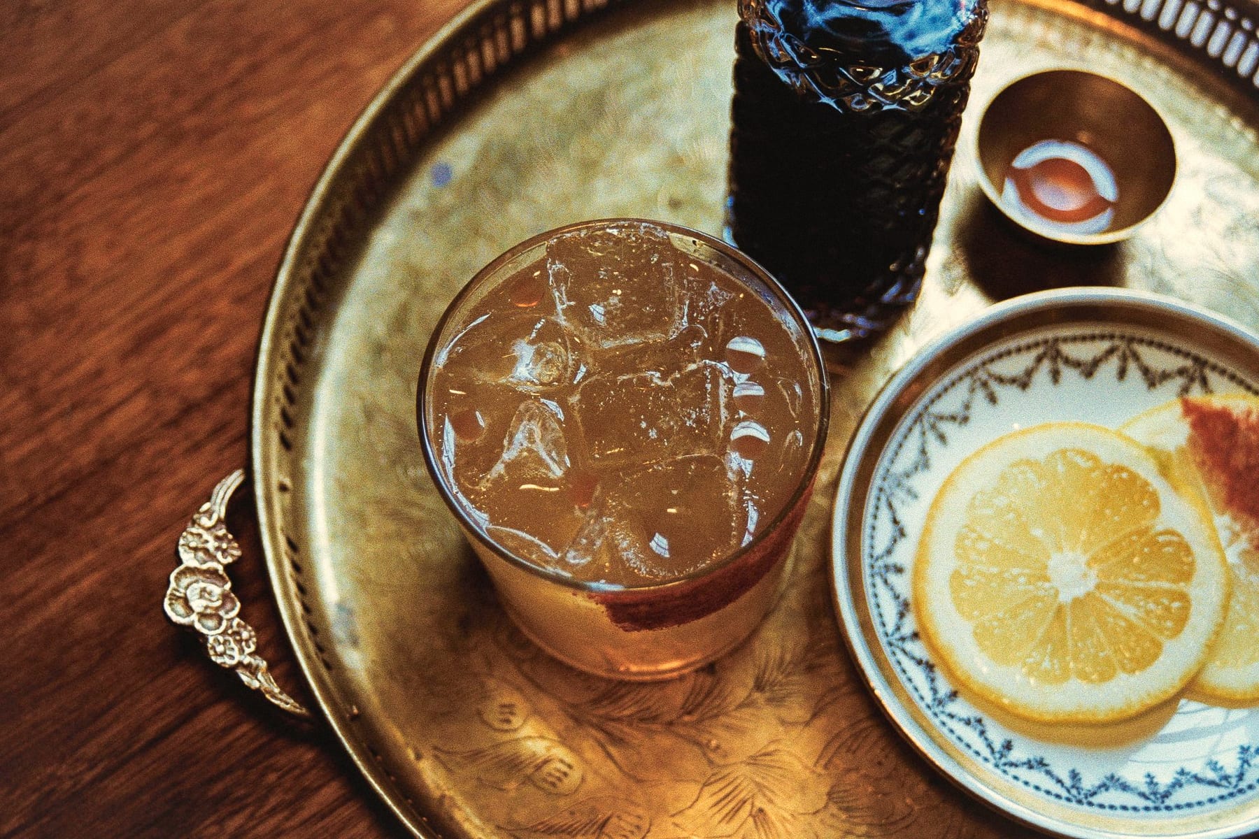 Iced amber drink on an engraved brass tray beside a cut-glass bottle and lemon slices