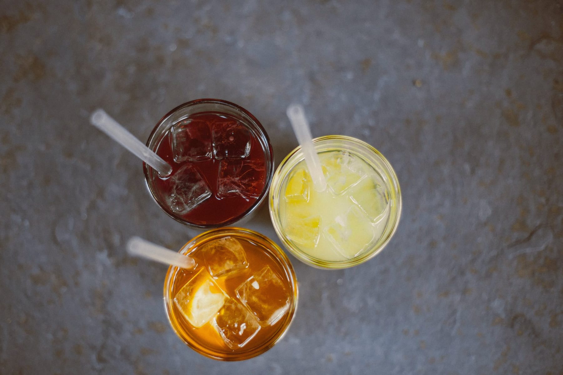Overhead view of red, orange and pale yellow iced drinks with straws on slate