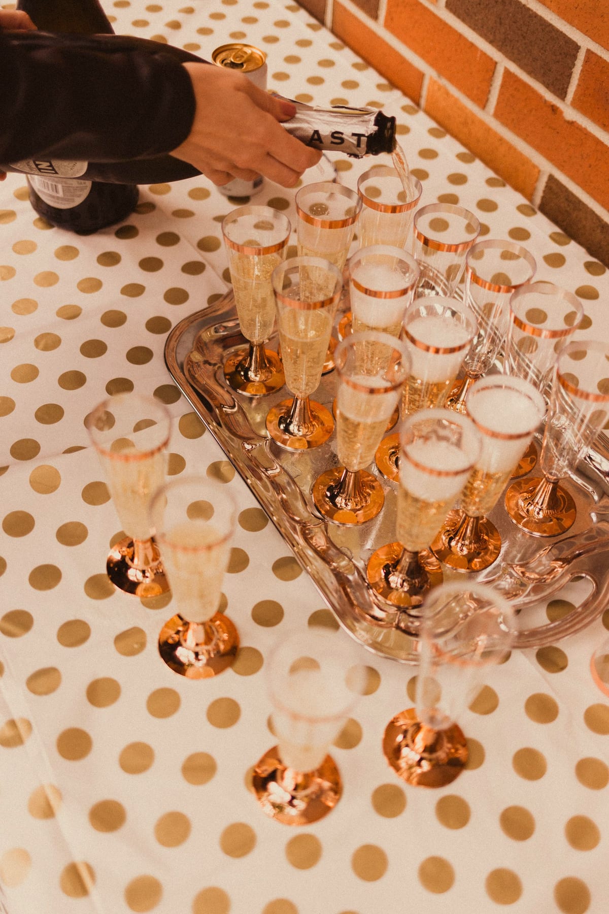 Hand pouring sparkling wine into rose-gold flutes on a gold polka-dot tablecloth