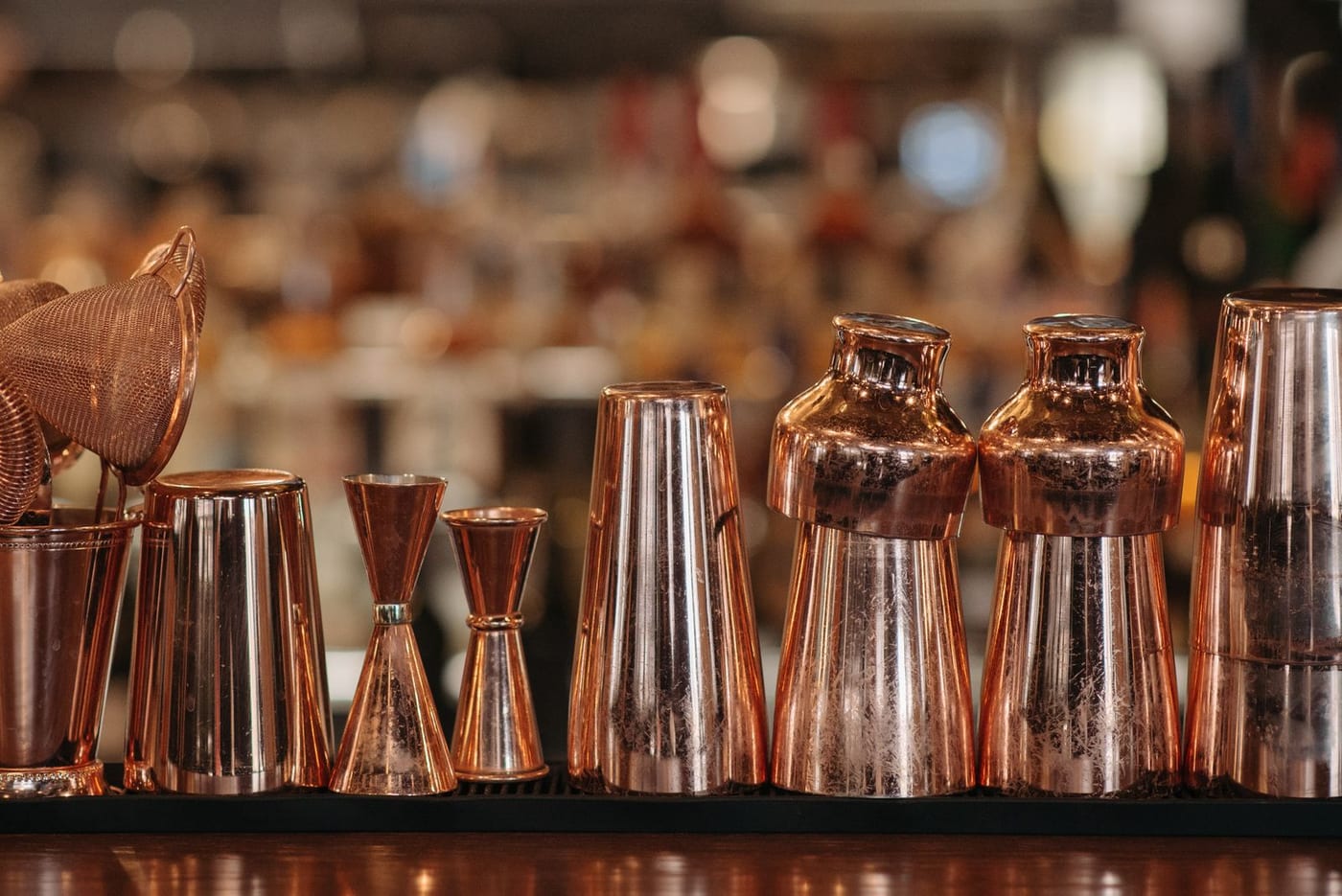 Copper cocktail shakers and jiggers lined up on a bar