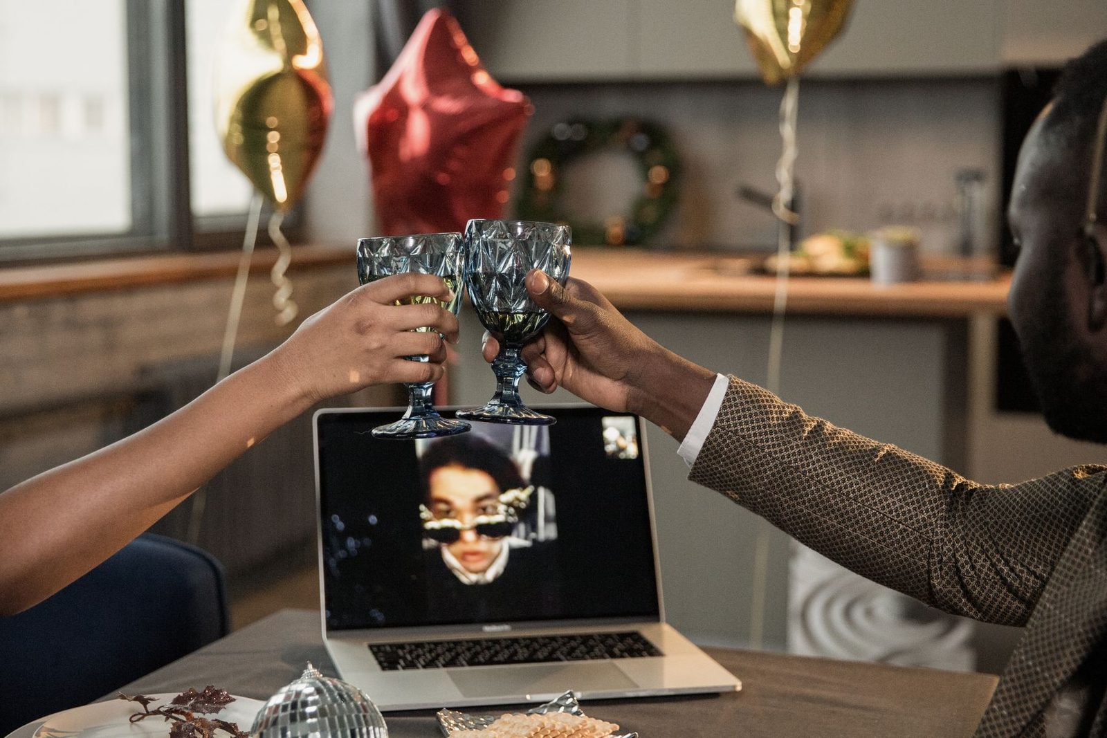 Two friends clinking glasses in front of a laptop on a video call