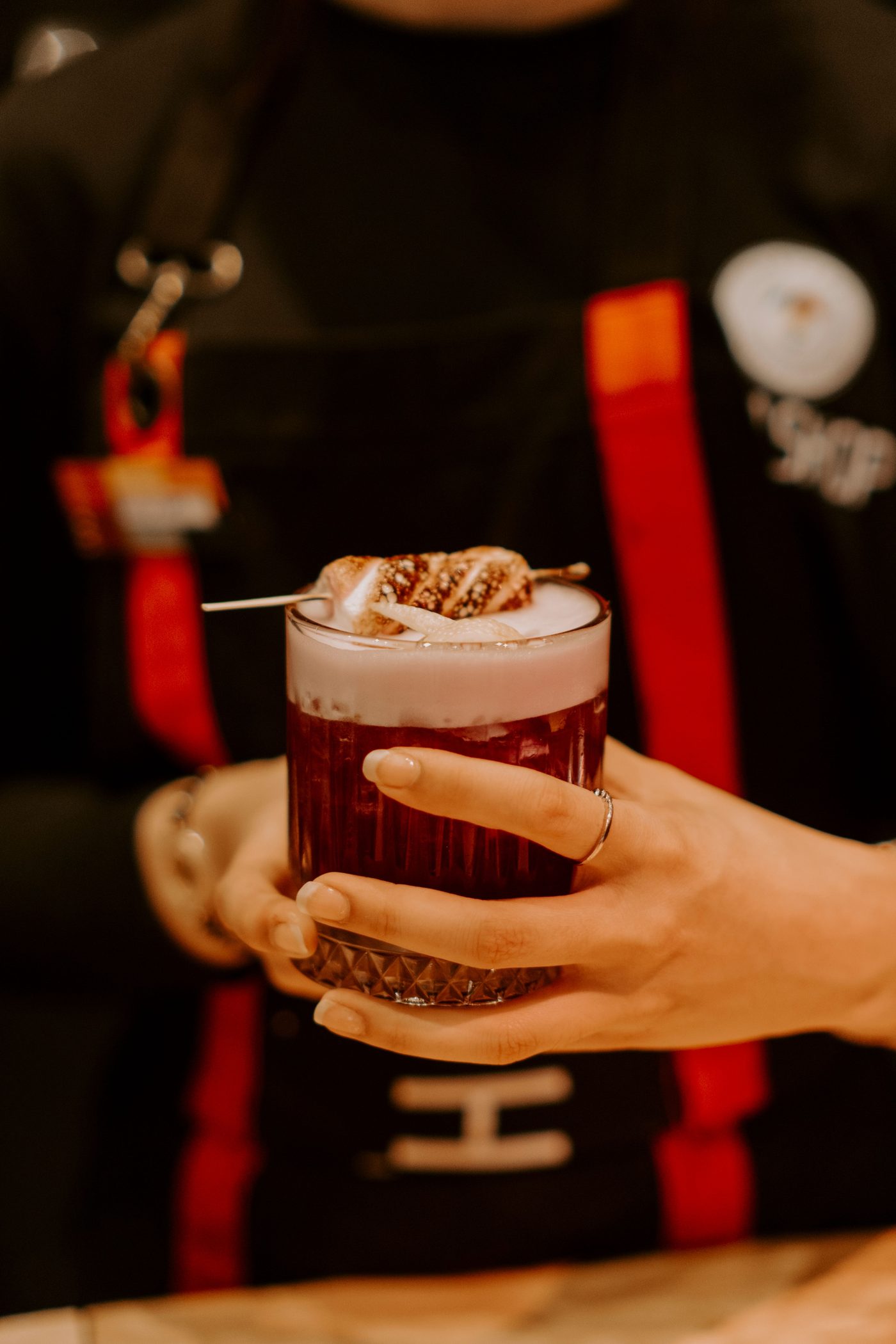 A bartender in an apron serving a cocktail topped with foam and a garnish