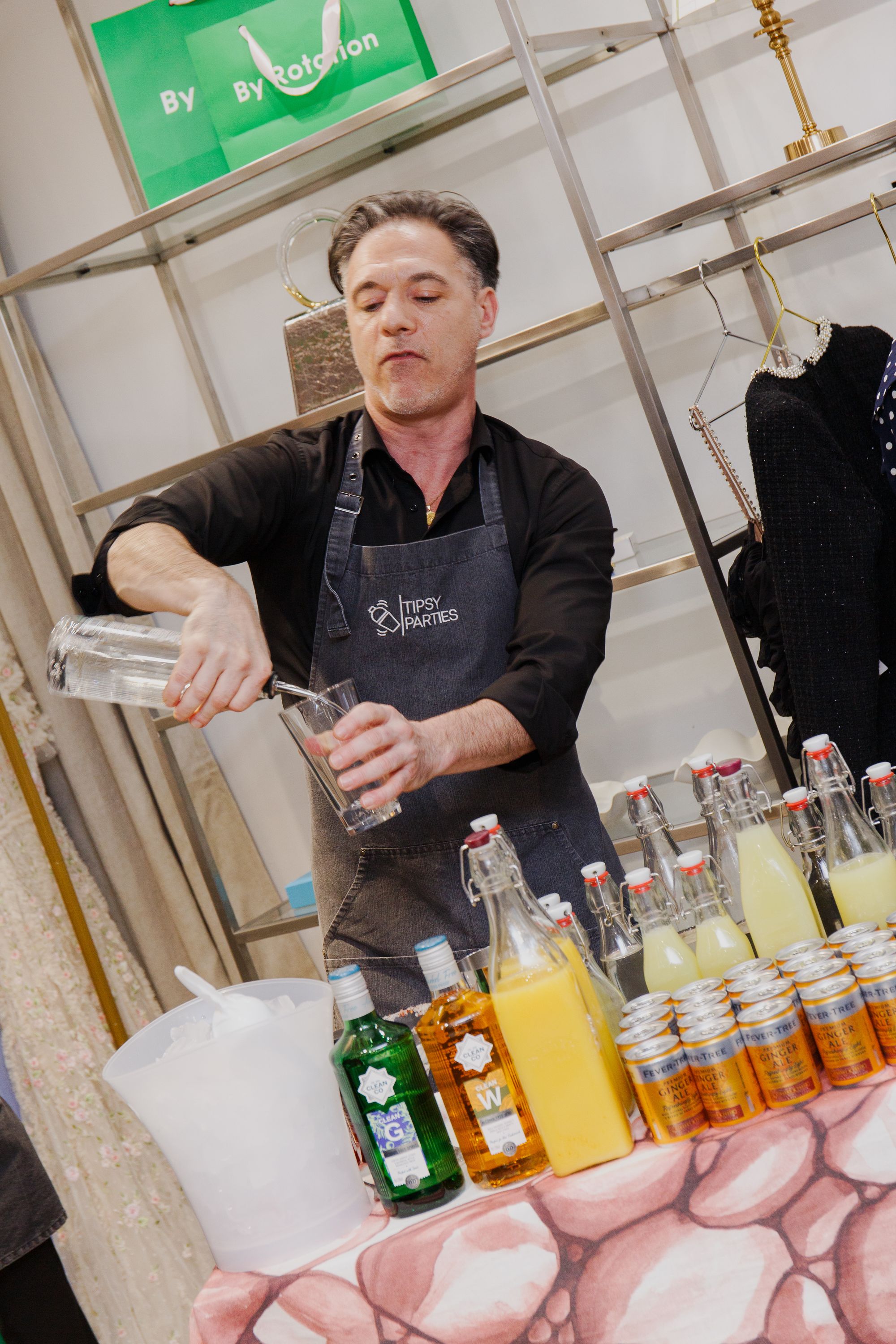 A Tipsy Parties mixologist in a branded apron pouring a drink behind a table of spirits, juices and ginger beer