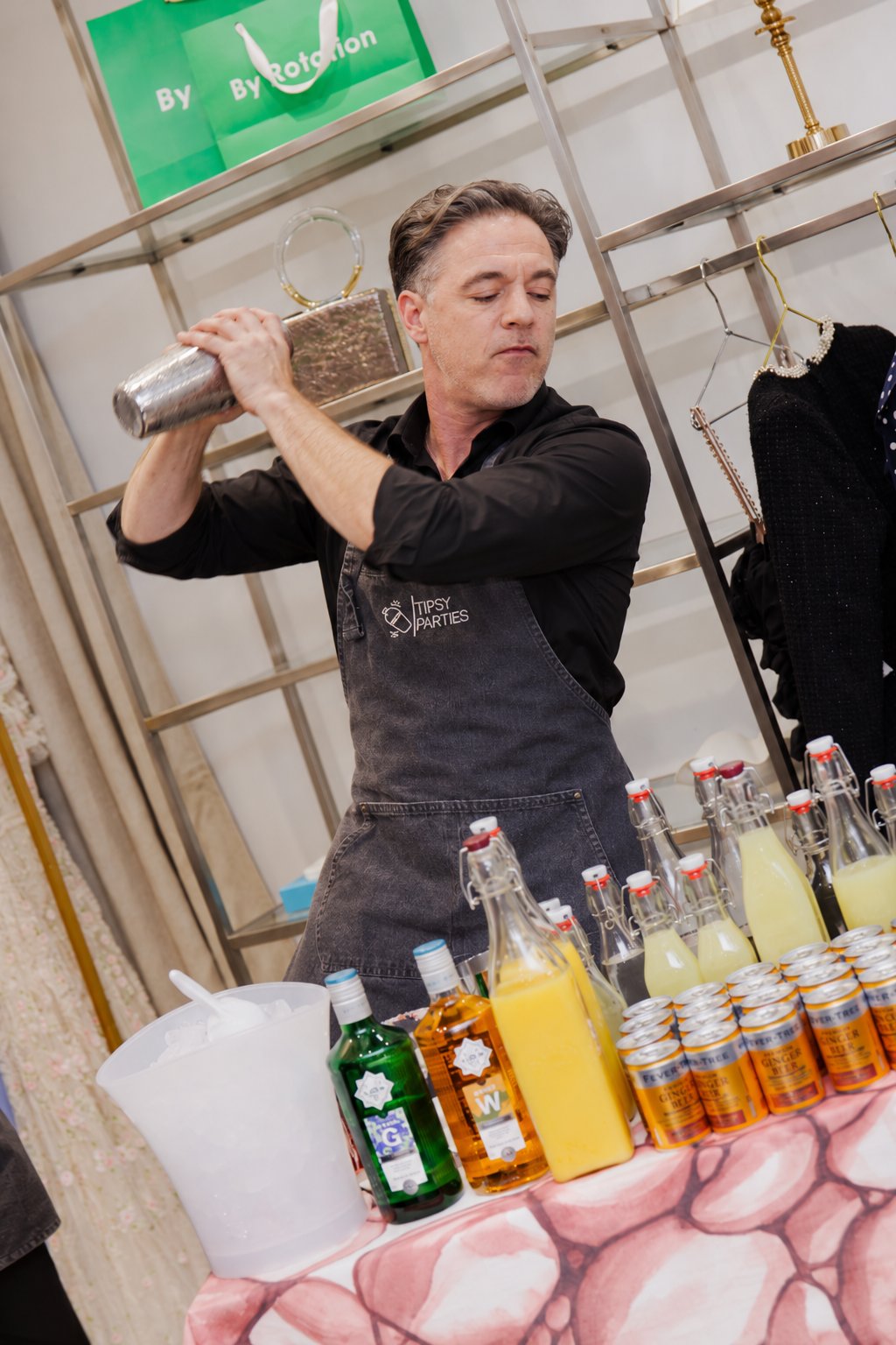 The Tipsy Parties mixologist shaking a cocktail shaker above his shoulder behind the drinks table