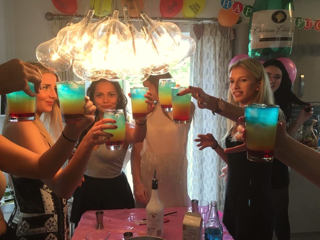 Friends holding up layered blue and orange cocktails under a glass chandelier
