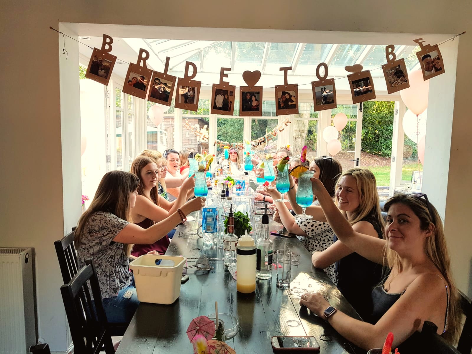 Hen party raising cocktails in a conservatory under a Bride to Be banner