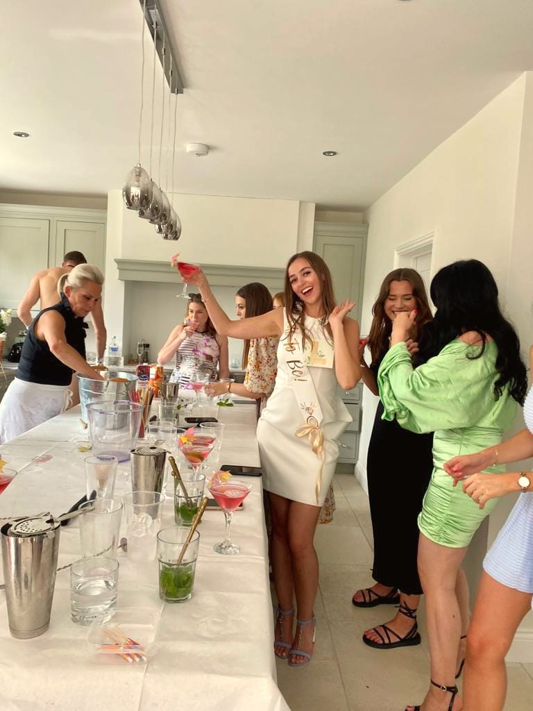 Hen party in a kitchen, the bride in white laughing with a cocktail