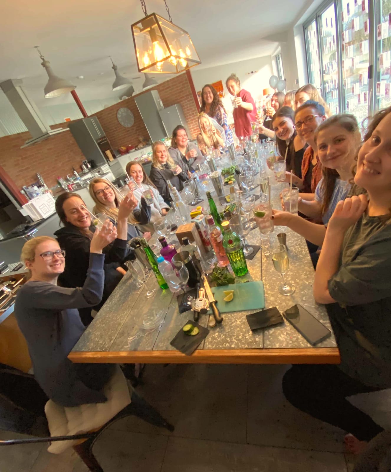 Group at a long kitchen table raising gin and tonics during a cocktail class