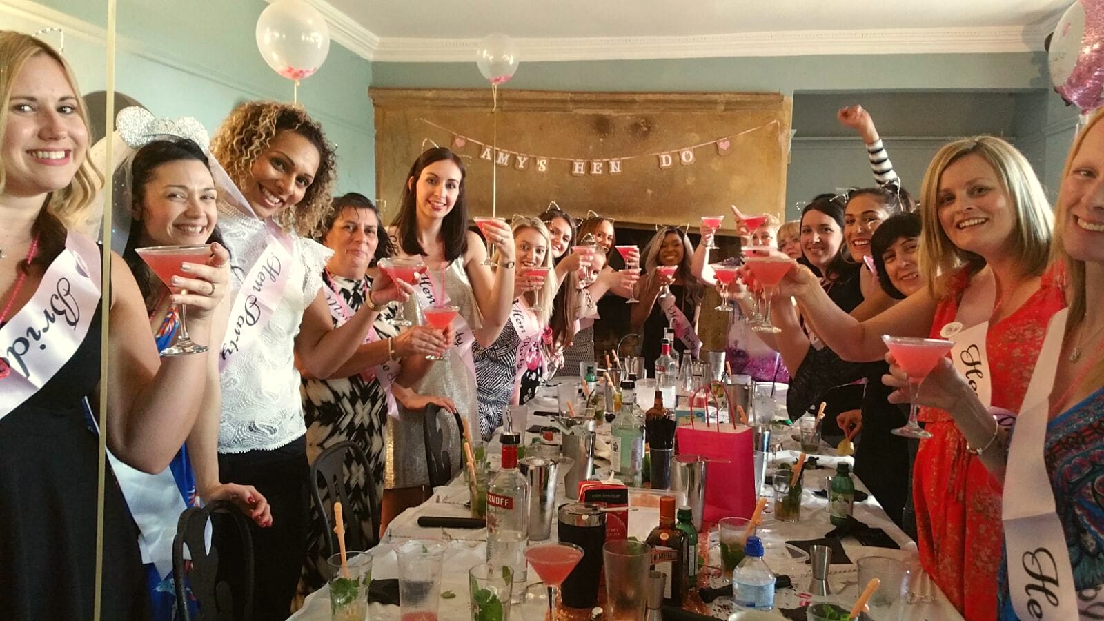 A hen party at a long table toasting with pink cocktails at a Tipsy Parties class