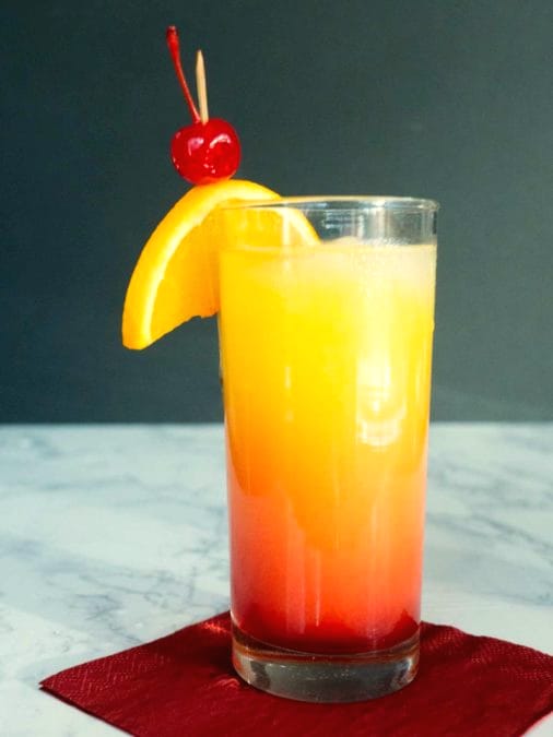 Orange-to-red layered cocktail in a highball with an orange slice and a cherry