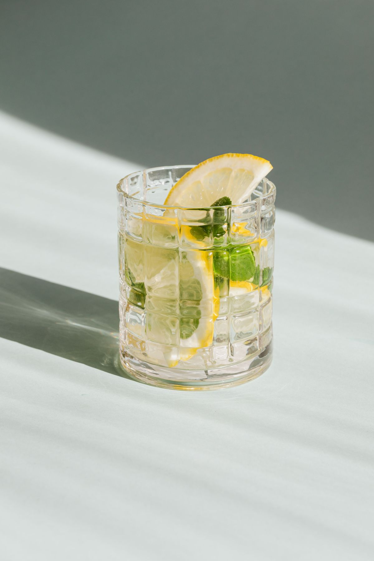 A glass of gin with lemon and mint on a sunny white table