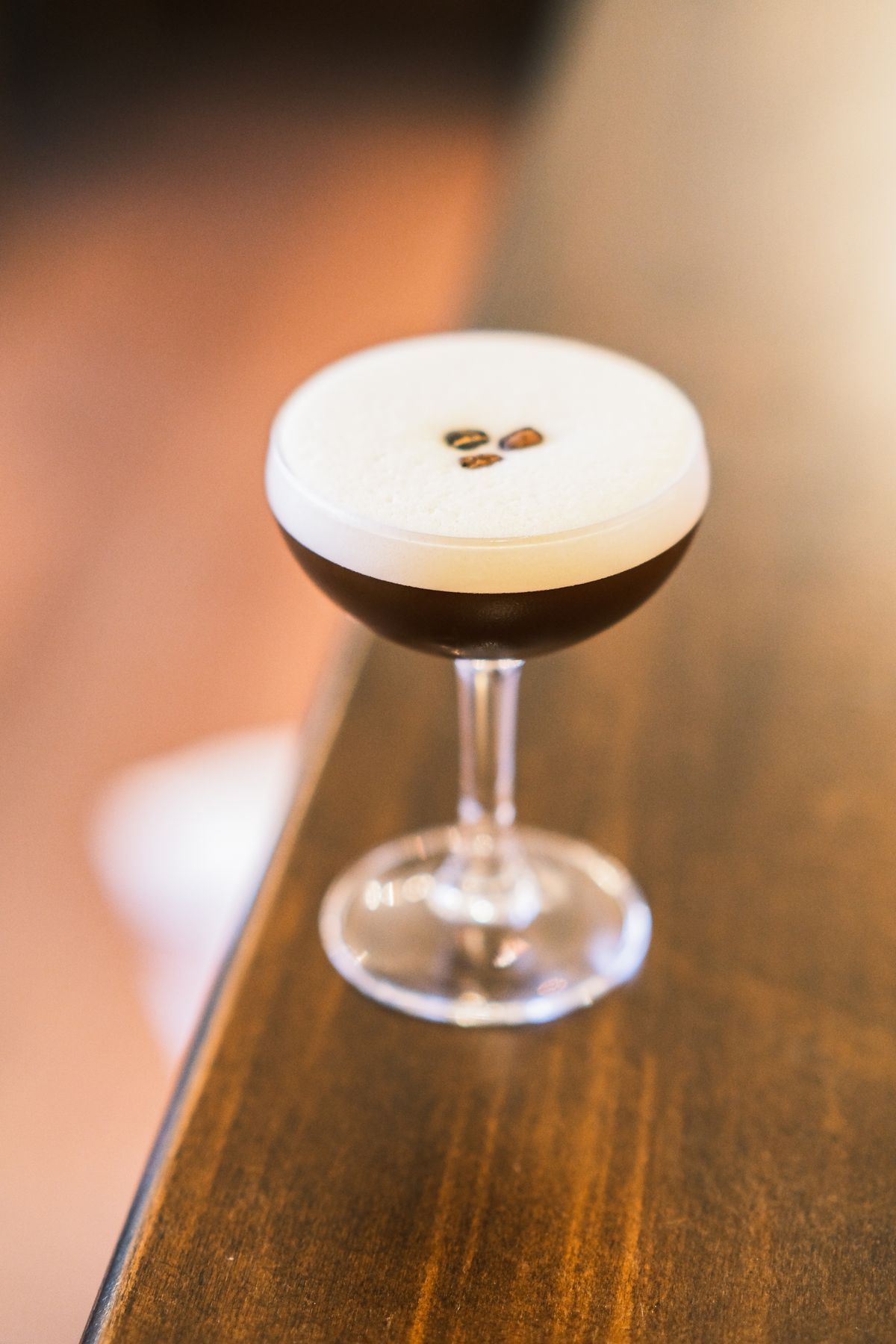 An espresso martini topped with coffee beans on a wooden bar