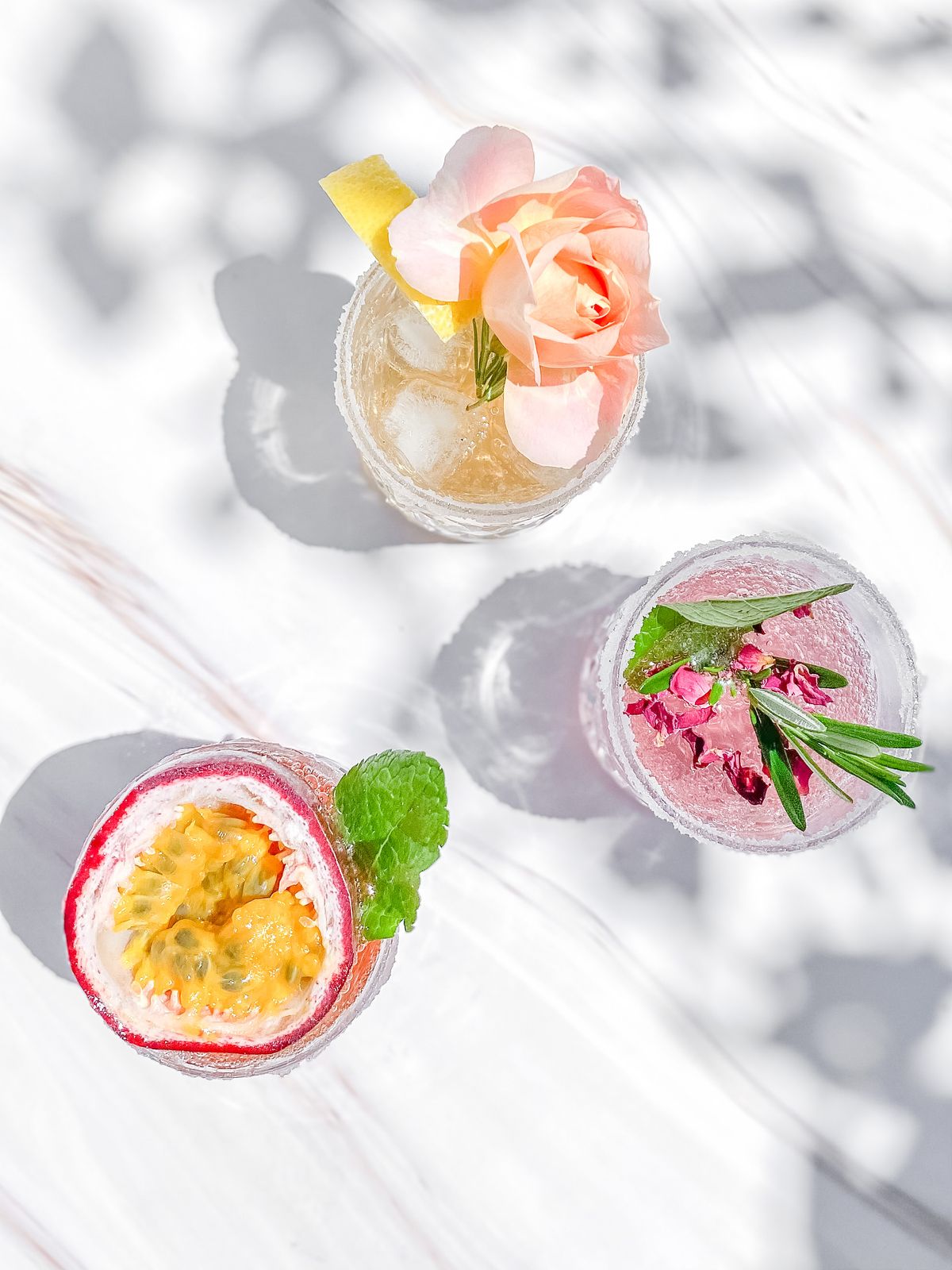 A passionfruit mocktail and a pink drink seen from above on white, in bright sunlight