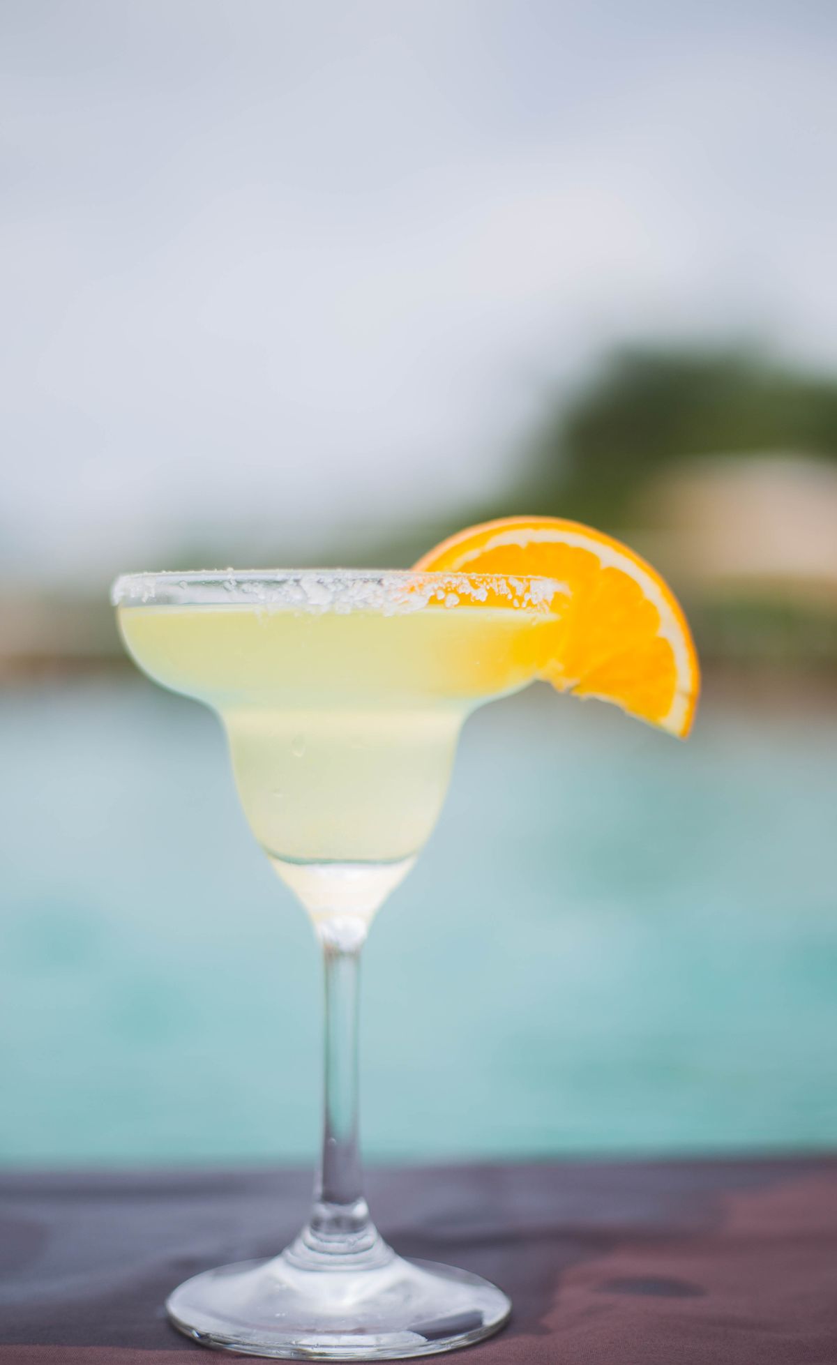 A margarita with an orange slice beside a swimming pool