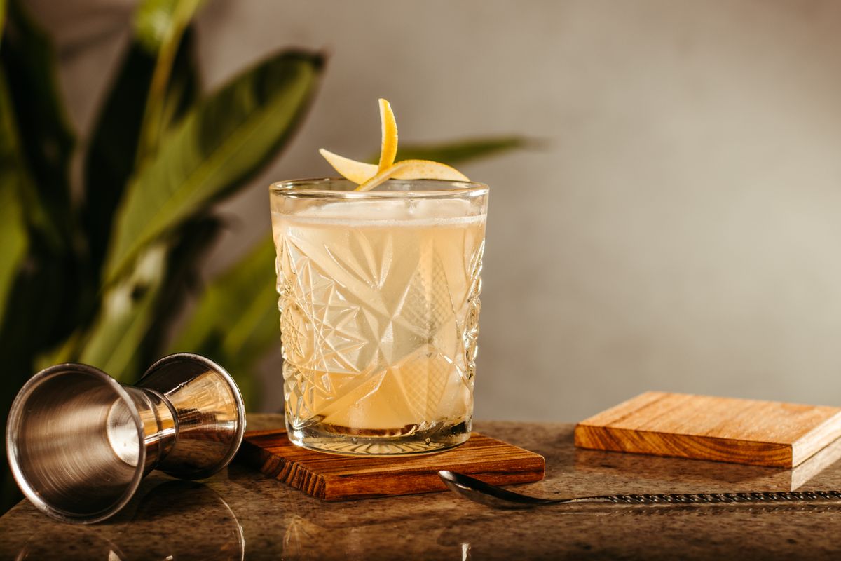 A whisky sour with a lemon twist on a bar counter
