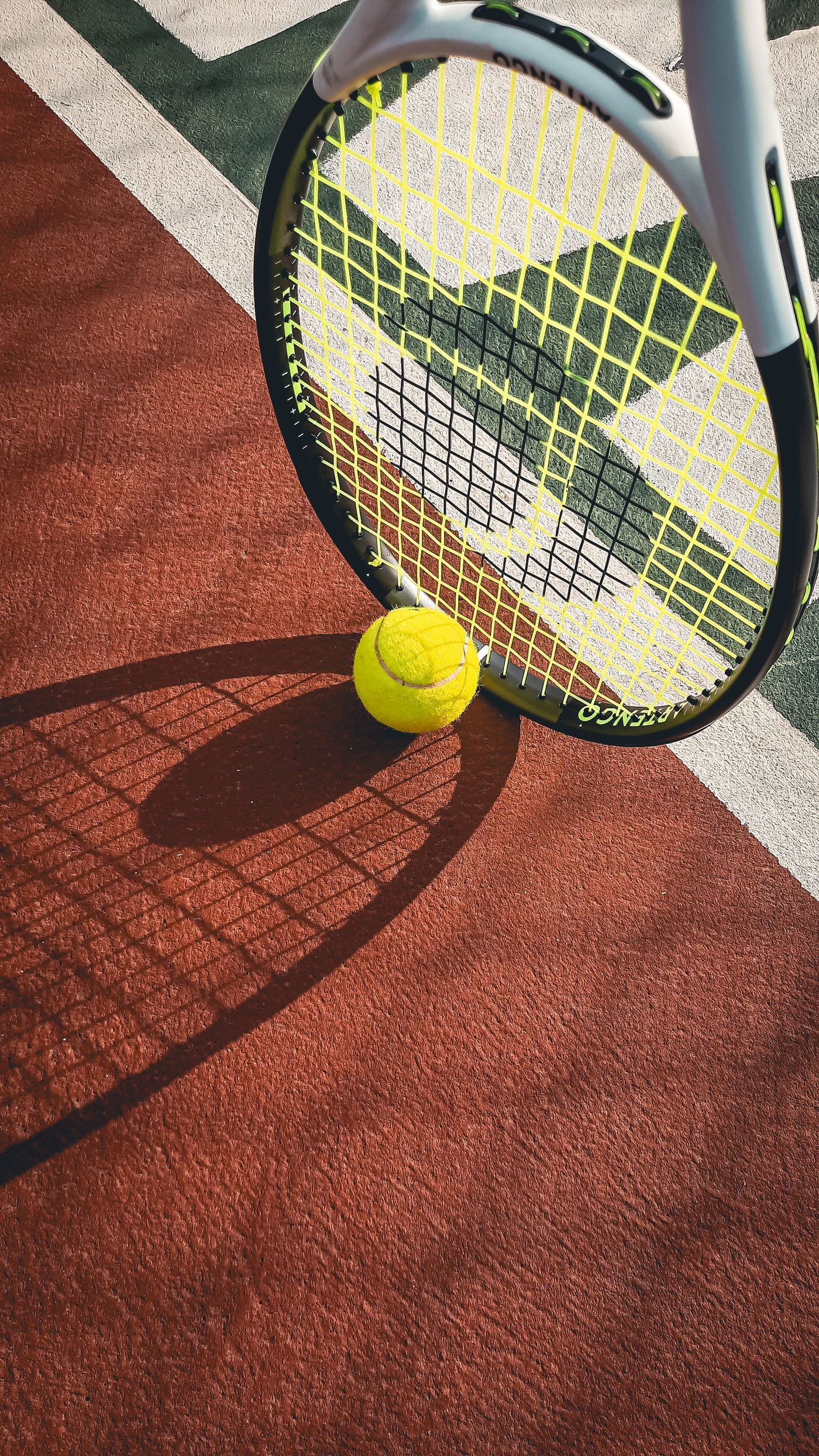 Close-up of a tennis racket and ball casting shadows on a sunlit court