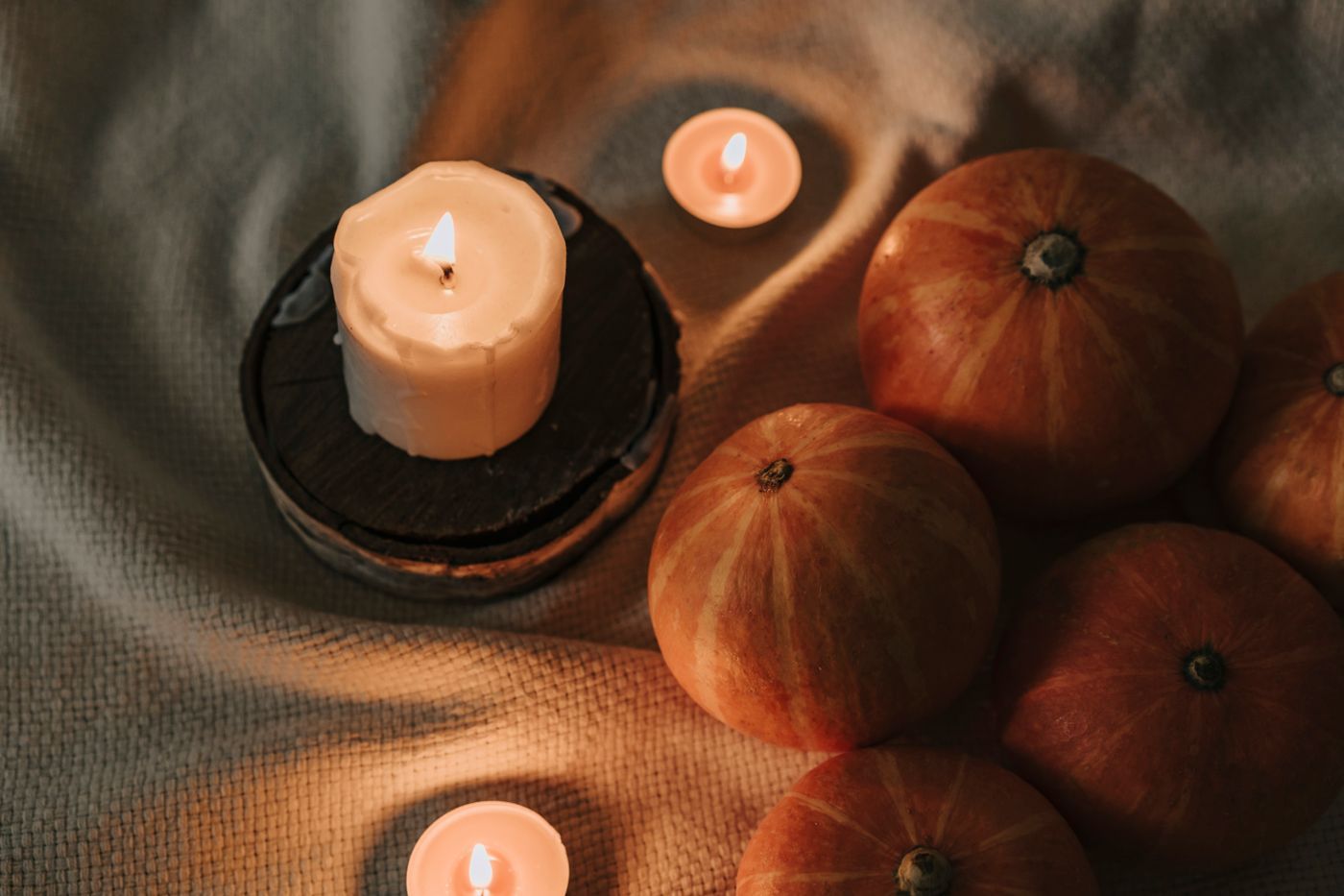 A warm autumn scene featuring lit candles and pumpkins on a cozy fabric