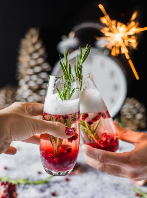 2 christmas cocktails in hand clinking glasses together.