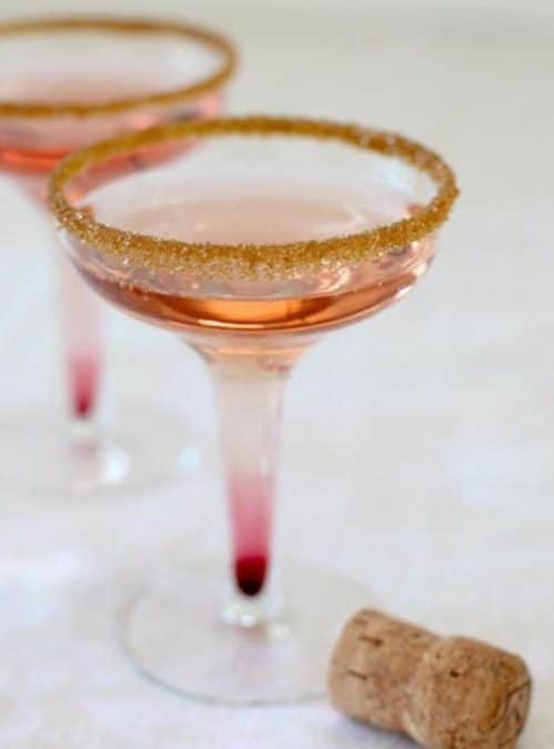 Gold sugar rimmed cocktails in a coupe glass with a discarded champagne cork on the table.