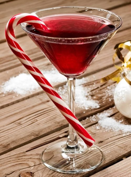 a red christmas cocktail in a martini glass with a candy cane hung on the side for garnish.