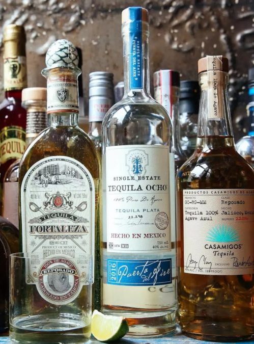 a selection of different tequila bottles on a bar shelf.