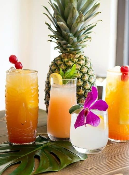 4 different tropical cocktails set in front of a fresh whole pineapple.